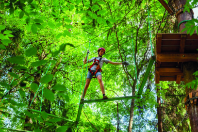 Une jeune femme fait de l'accrobranche sur un câble entre les arbres - Agrandir l'image, fenêtre modale