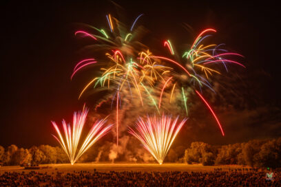 Feu d'artifice tirée dans une prairie avec des spectateurs assis dans l'herbe en pleine nuit. - Agrandir l'image, fenêtre modale