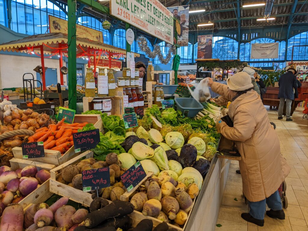 Vue intérieure des halles avec une personne qui achète des fruits et légumes. - Agrandir l'image, fenêtre modale
