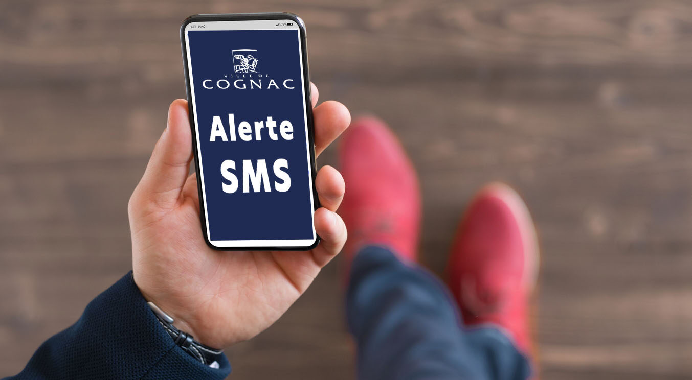Main qui tient un smartphone dans lequel est écrit Alerte SMS avec le logo de la Ville de Cognac