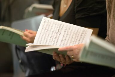 Mains de chateurs qui tiennent des partition de musique.